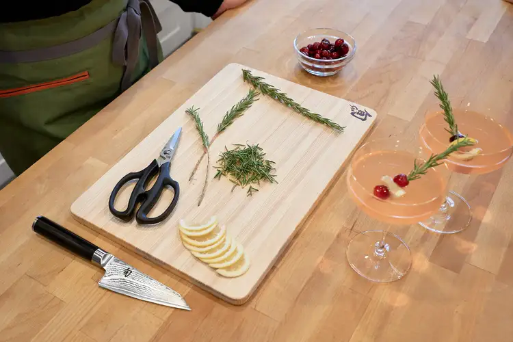 A neatly arranged cutting board with rosemary sprigs, stripped needles, lemon slices, and herb shears.