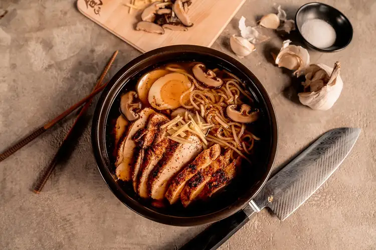 A bowl of fresh ramen, filled with sliced chicken and a soft boiled egg, is shown from the top down.