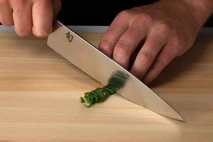 Chef slicing rolled basil leaves into thin ribbons using a Shun knife, demonstrating chiffonade technique.