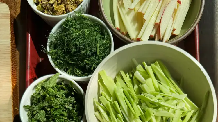 Bowls full of sliced vegetables and herbs that will be mixed together for the slaw.