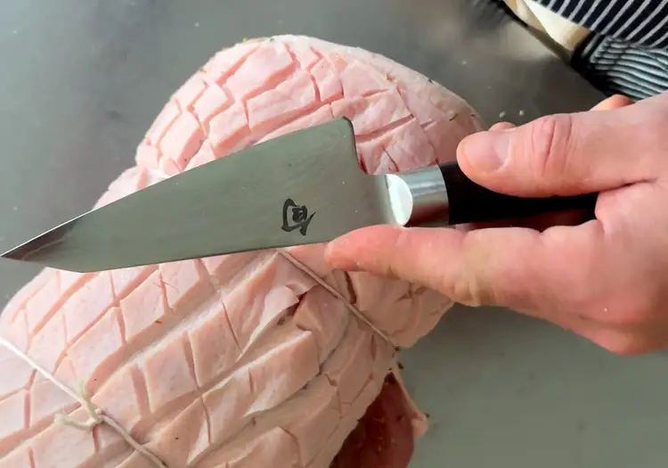 Chef Avery Hardin holds his Shun Classic Multi-Prep over a wrapped, scored roll of meat.