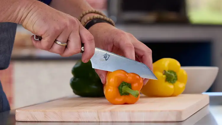 Close-up of a hand slicing a yellow bell pepper with a Shun Kanso Asian Multi-Prep knife. Click to shop this knife.