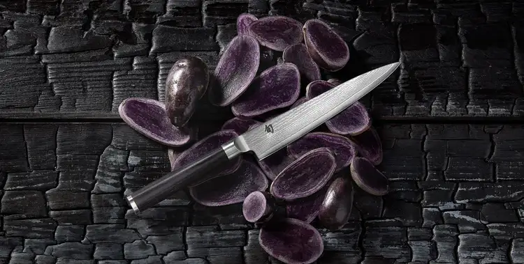 A Classic 6" Utility Knife is shown lying on top of thinly sliced purple potatoes. Click to shop.