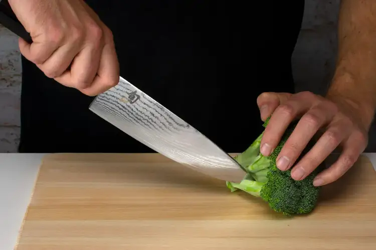 A single broccoli floret is being separated by cutting into the branching stem with the knife tip.