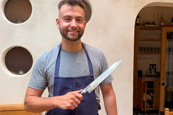Chef Vitor Mendes smiling and holding a Shun Dual Core Yanagiba knife in a bright, modern kitchen at Theodora. Click to watch his interview.