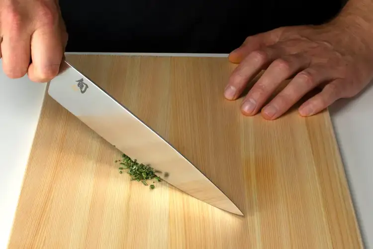 Overhead view of a chef mincing herbs using a Shun knife and controlled rocking technique.