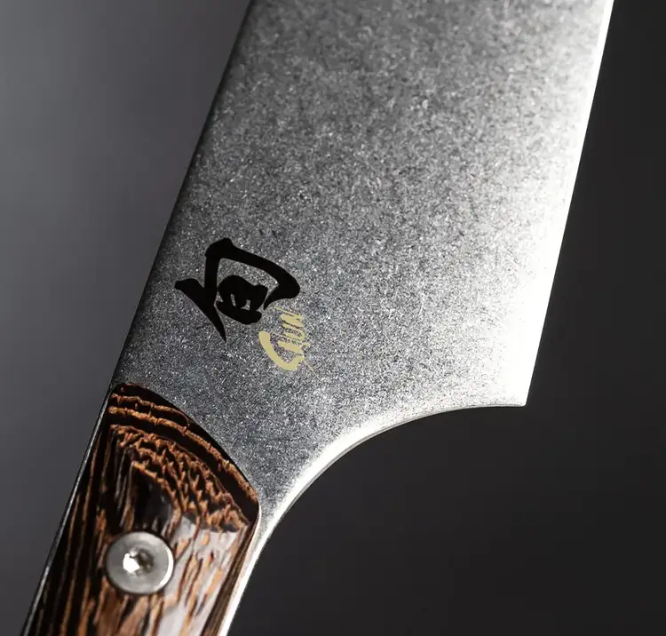 Close-up of the Shun logo on the Kanso knife’s rustic stonewashed blade near the handle, showing fine detail and finish.