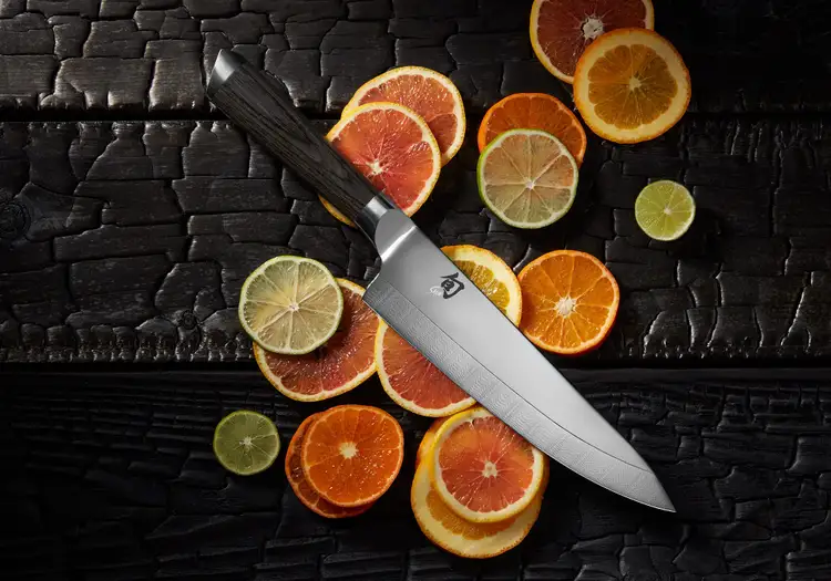 Shun Kagerou 8-inch Chef's Knife displayed on charred black wood with sliced citrus fruits. Click to shop Kagerou at Sur La Table.