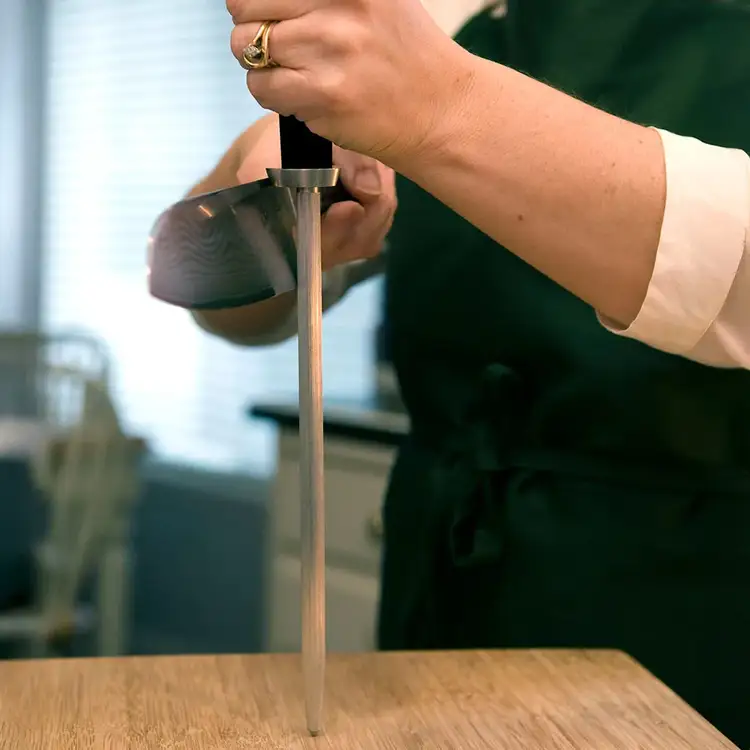 Home cook honing a Shun knife with a honing rod on a wooden cutting board, showing proper edge maintenance technique.