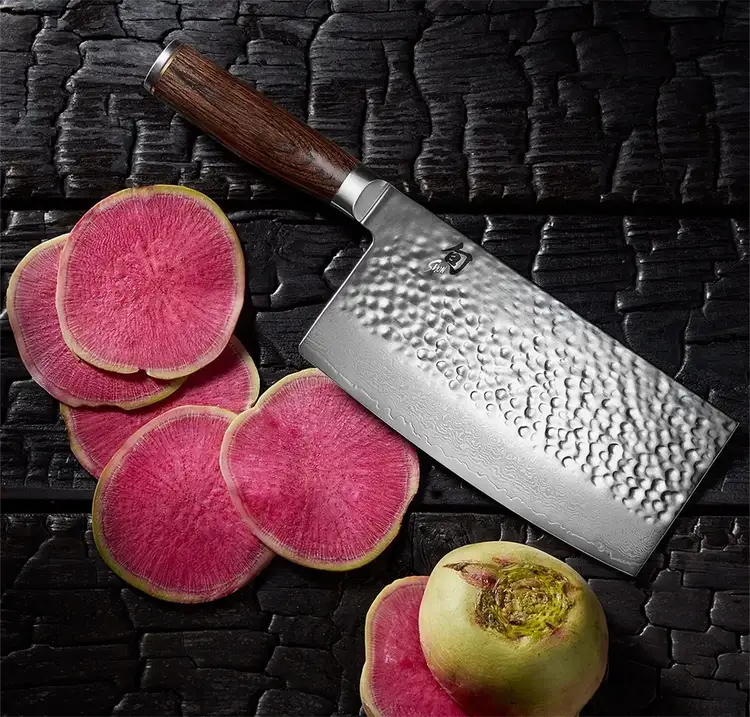 A Premier Vegetable cleaver lies next to finely sliced watermelon radishes.