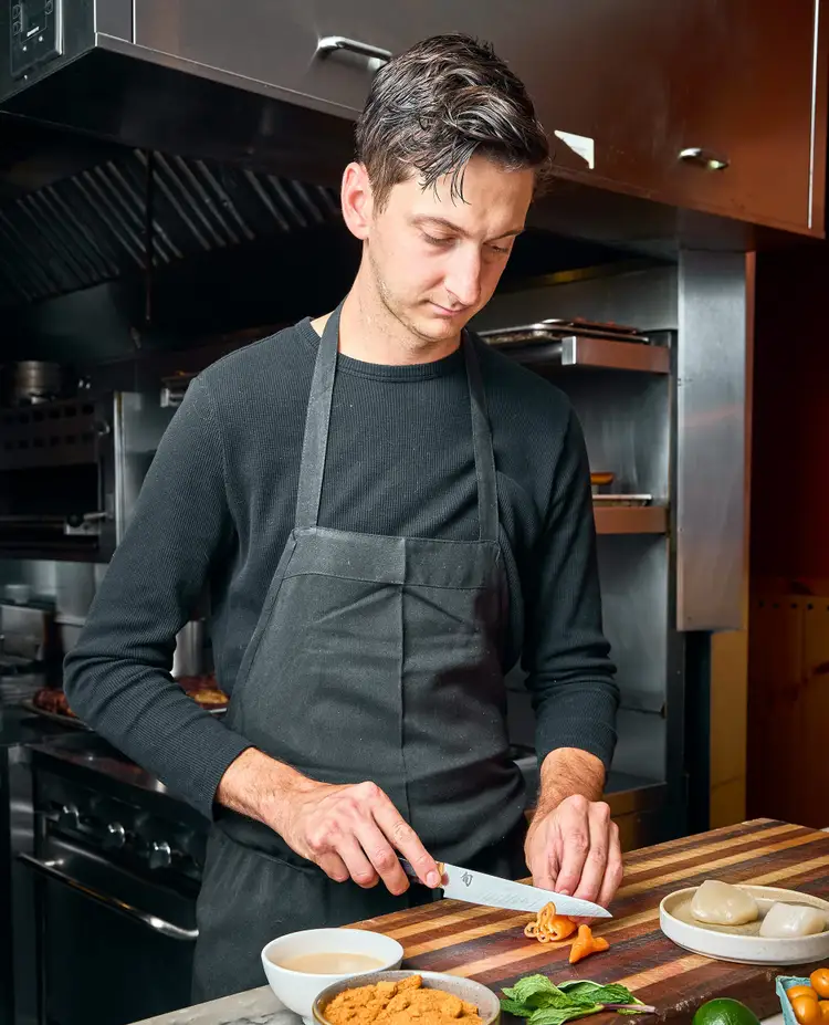 Chef Nate Hobart slicing habanada peppers on a wooden cutting board using the Shun Dual Core 6" Utility Knife in the kitchen at Morcilla.