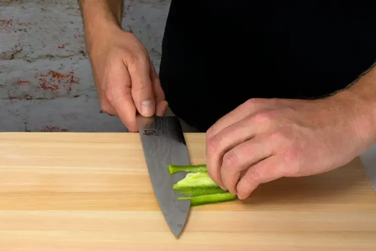 The pepper is laid flat, and the hand begins trimming away the white ribs inside with a Shun Classic Chef’s Knife.