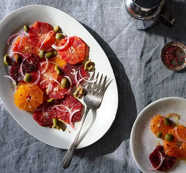 Sliced citrus on a plate with green olives and onions