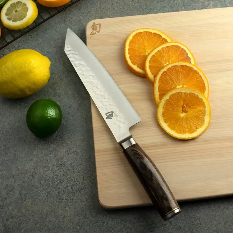 Shun Premier Kiritsuke knife with walnut handle on a cutting board next to sliced citrus fruits. Click to shop.