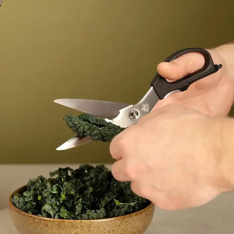Kitchen shears cutting curly kale leaves over a bowl.