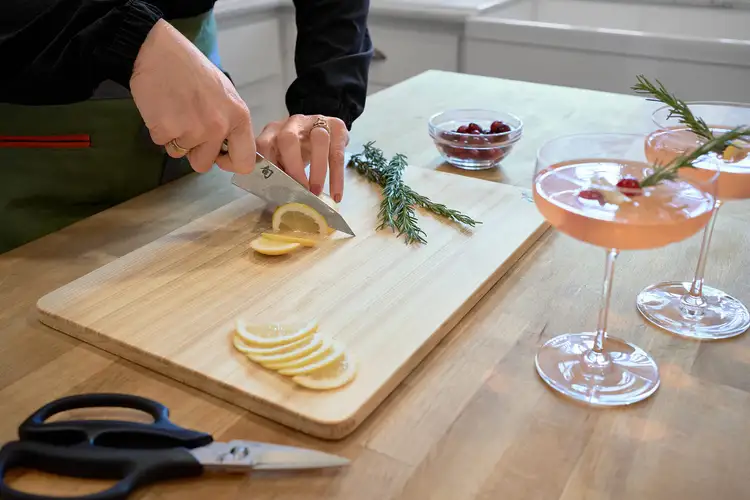 Slicing a lemon into thin half-moon slices with a Shun knife on a wooden cutting board.
