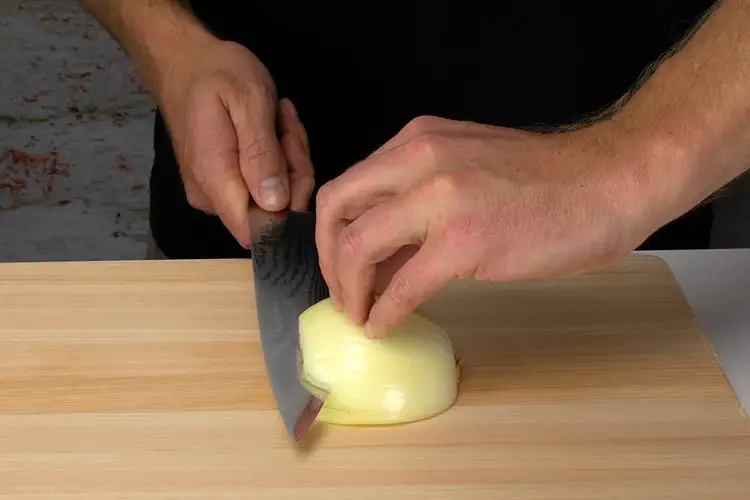 Chef making horizontal cuts into the onion, stopping just before the root to keep the layers together.