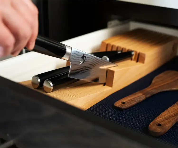 Shun knife being placed spine-first into an in-drawer wooden knife tray, showing proper knife storage to protect the blade.