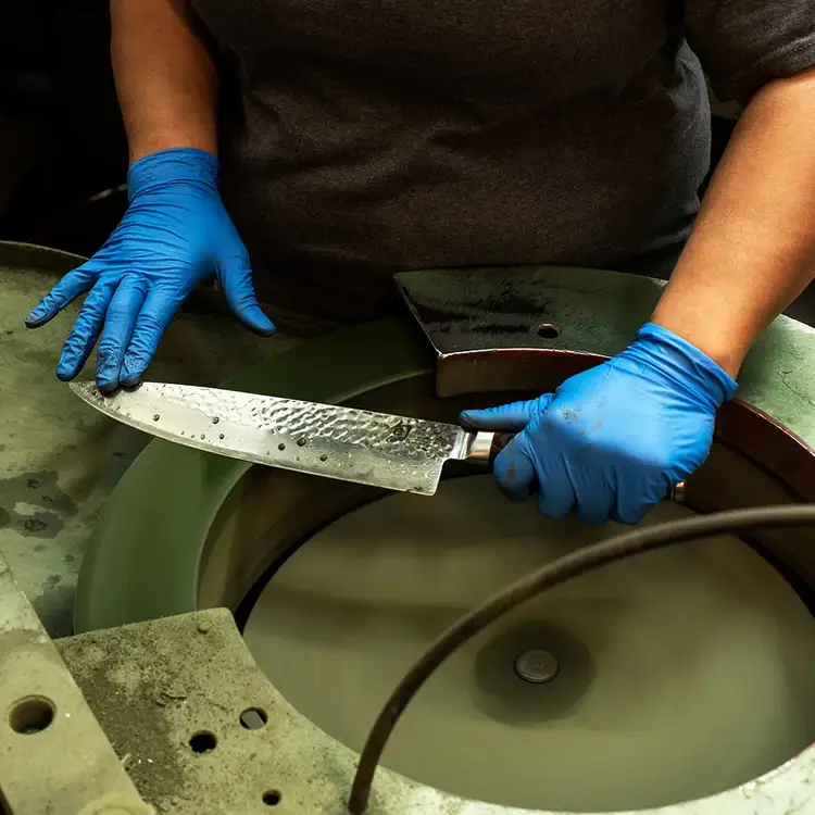 Shun knife being professionally sharpened on a large rotating stone, illustrating factory sharpening and blade restoration.
