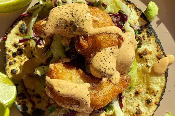 Close up of beer battered shrimp, covered in crema, sitting on a grilled tortilla.
