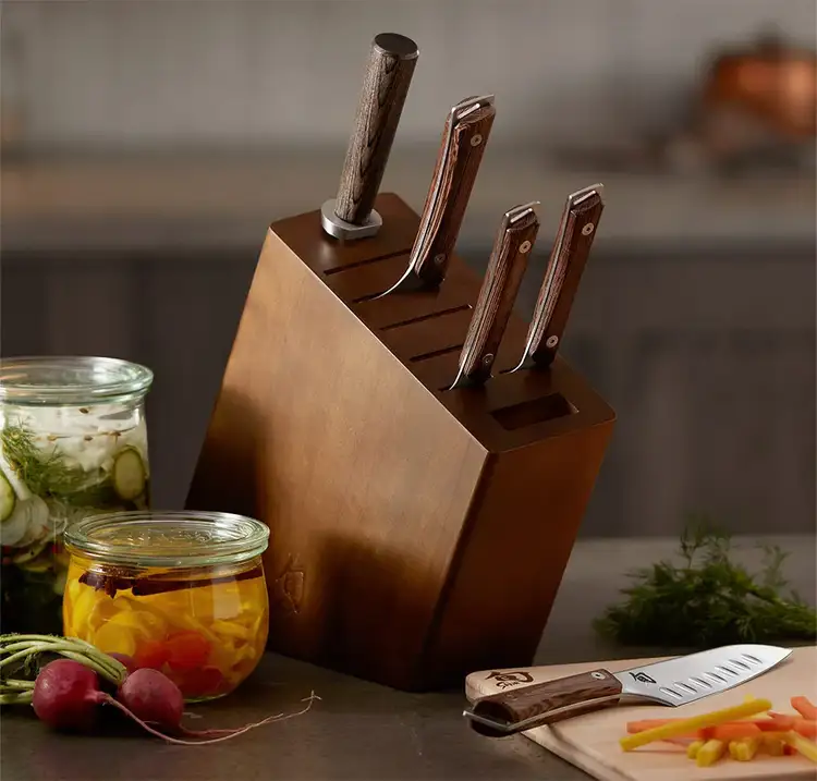 Shun Kanso knife block set with knives inserted, surrounded by pickled vegetables and fresh produce, emphasizing everyday utility and design cohesion.