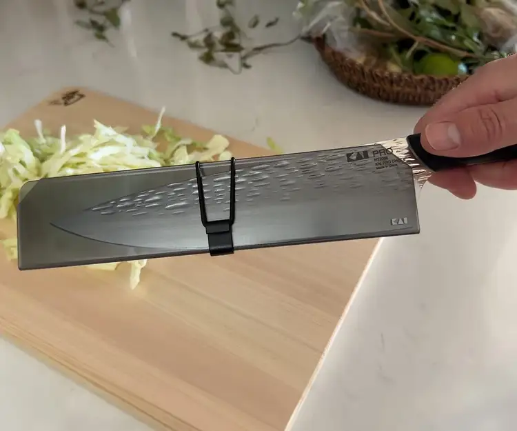 Shun knife protected with a blade guard in front of a Hinoki cutting board, demonstrating safe storage and edge protection.