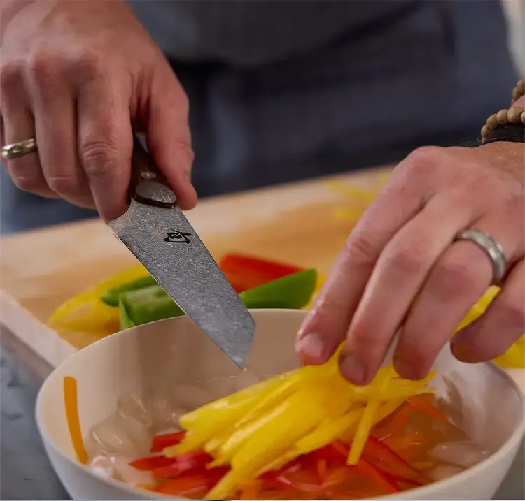A cook using the Shun Kanso Asian Multi-Prep Knife to prepare julienned vegetables, demonstrating precision control and blade sharpness.