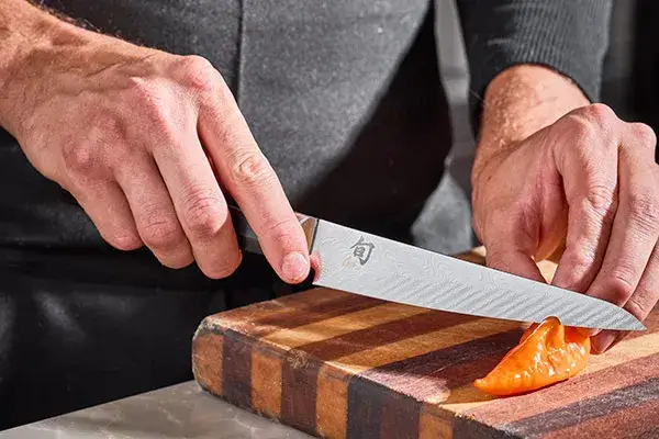Close-up of the Shun Dual Core 6” Utility Knife as Chef Nate Hobart precisely slices havanada peppers on a striped butcher block.