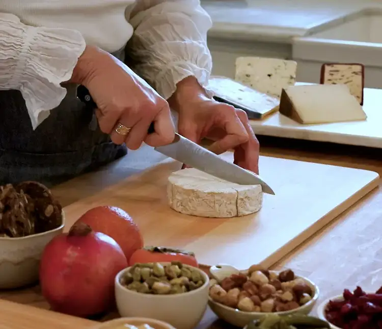 Slicing into a round of Camembert using a Shun Kazahana 6" utility knife, surrounded by cheese and fresh fruit.