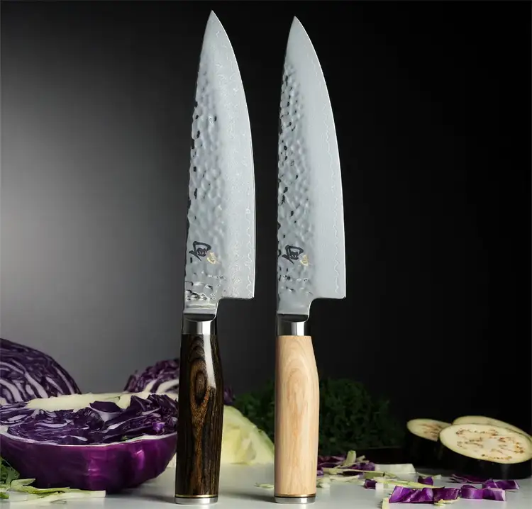 Image of two Premier Chef's Knives, one with a walnut and one with a blonde handle, standing vertically on a table.