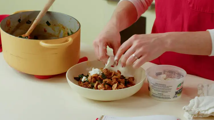 Chef Baz sprinkles buratta over her plate of pasta.