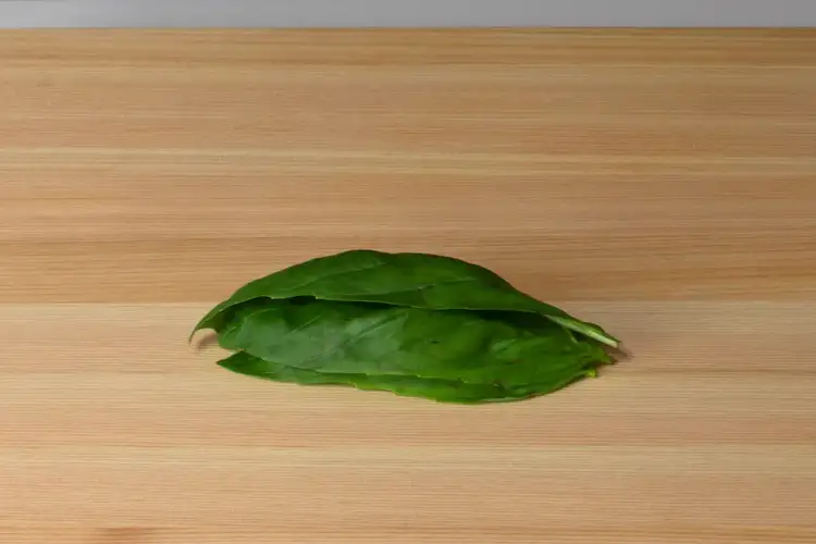 Basil leaves stacked and aligned on a cutting board, prepared for chiffonade slicing technique.
