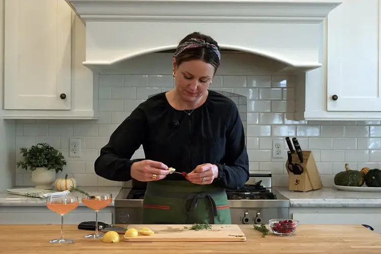 Threading a cranberry and lemon slice onto a rosemary sprig to create a cocktail garnish.