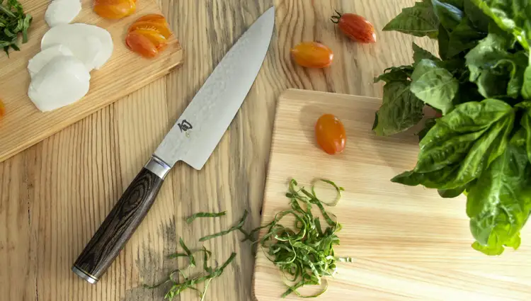 Shun Premier Chef’s knife on a wooden surface with fresh basil, tomatoes, mozzarella, and chiffonade-cut herbs. Click to shop the Premier Chef's Knife.