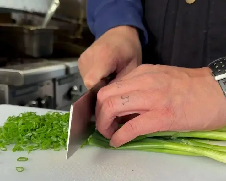 Close-up of Chef Paolo Campbell using a Shun Kanso Asian Utility knife to slice green onions.