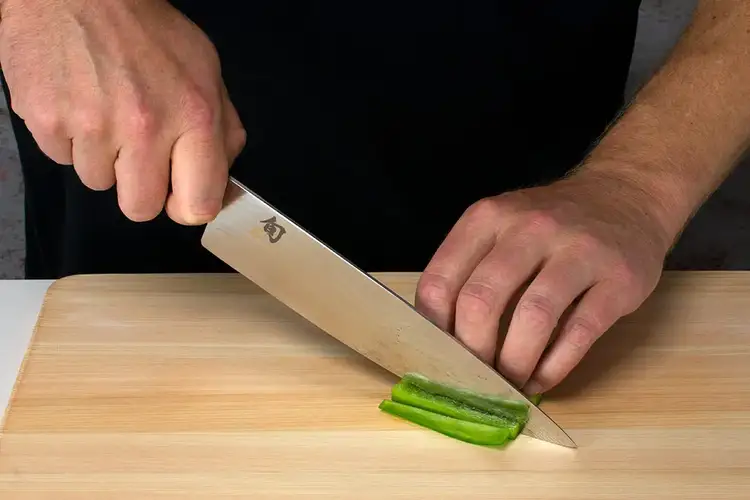 A clean pepper strip is being sliced into even segments with a downward slicing motion.