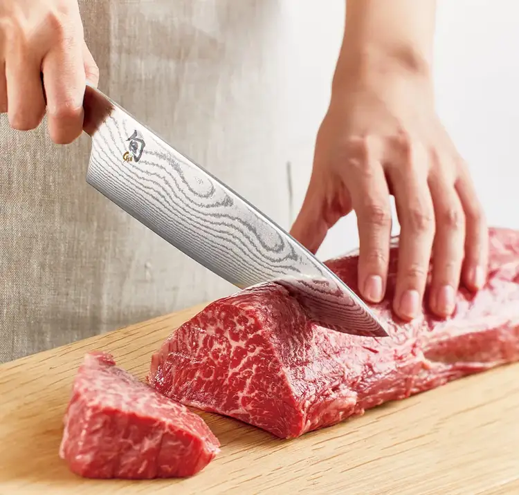 A chef slices a cut of meat with a Classic Chef's Knife.