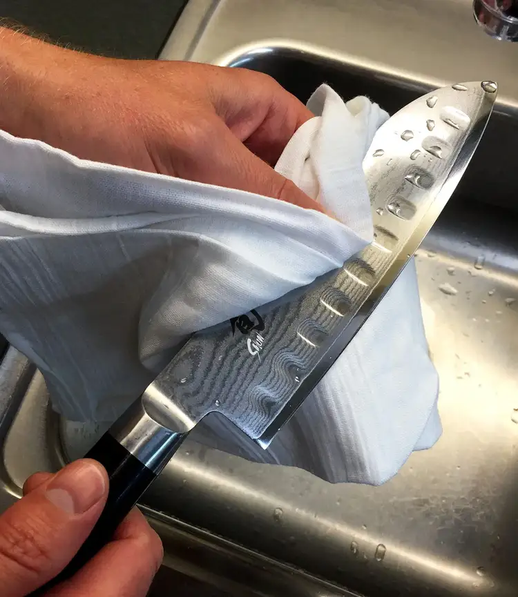 Hand drying a Shun knife with a clean towel after washing, emphasizing proper drying to protect the blade.