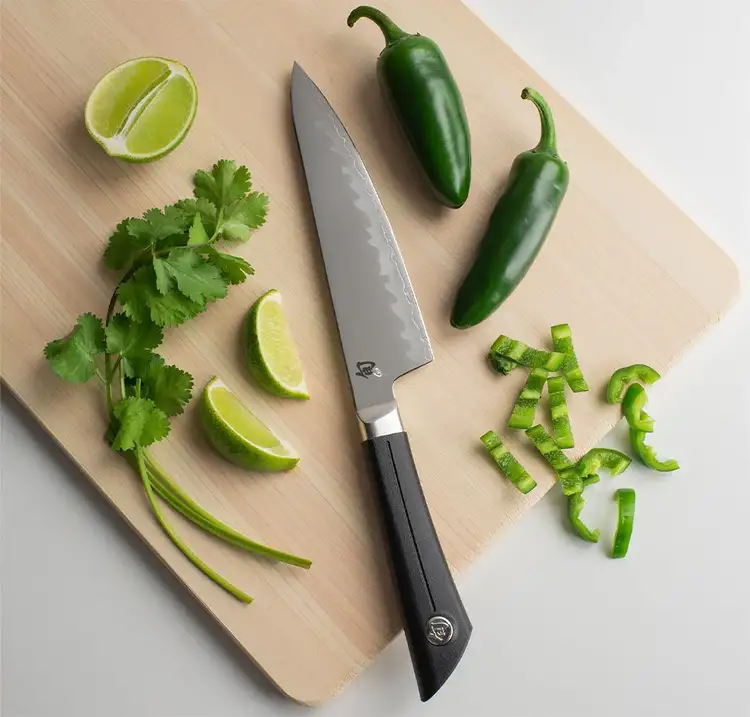 Shun Sora Chef’s Knife laid on a cutting board surrounded by jalapeños, lime wedges, and cilantro, demonstrating versatility in everyday kitchen prep.