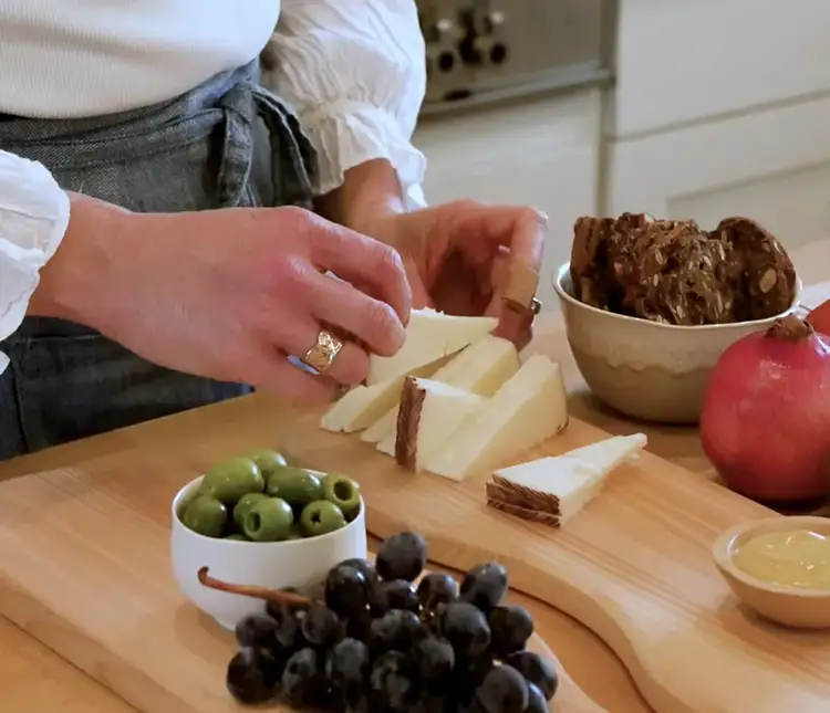 Arranging triangular slices of Manchego cheese in a zigzag pattern next to olives and grapes.