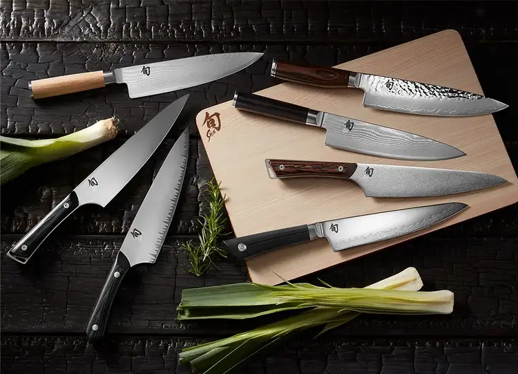 A grouping of Shun Chef's Knives lying on a table around a Hinoki cutting board.
