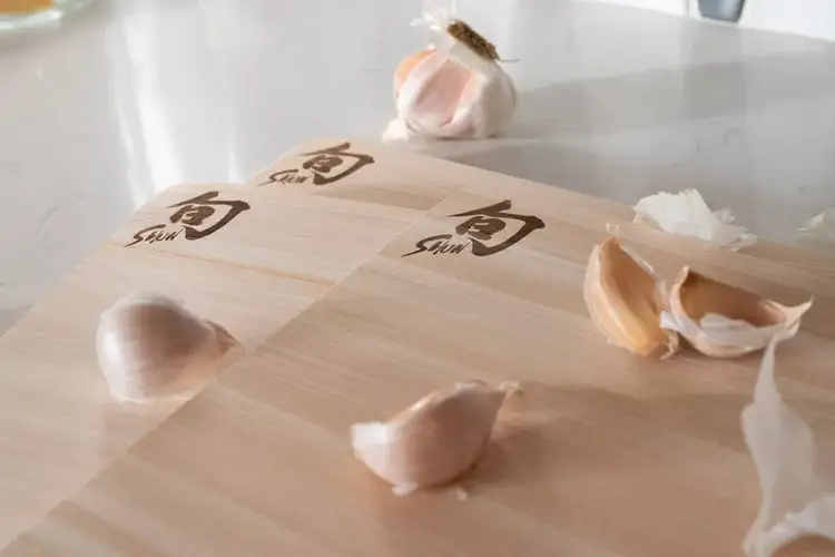Shun-branded hinoki cutting boards with garlic cloves, highlighting ideal surfaces for knife edge protection. Click to shop Hinoki boards.