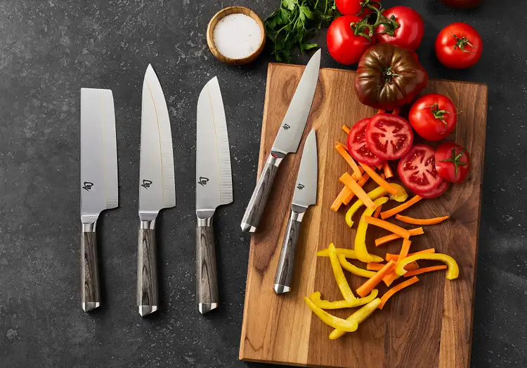 Complete Shun Kagerou knife series displayed with sliced tomatoes, peppers, and carrots on a wooden cutting board. Click to shop the collection at Sur La Table.