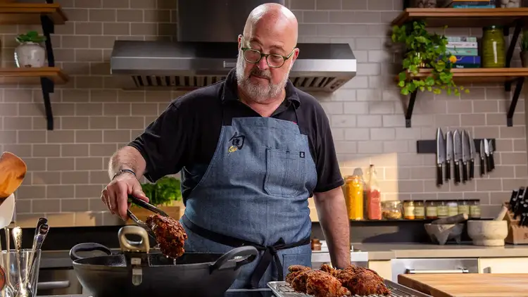 Chef Andrew Zimmern removing fried chicken pieces from a wok with tongs
