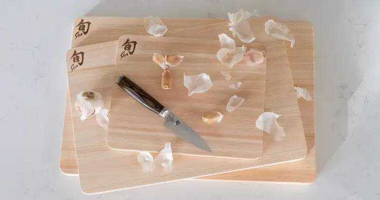 Shun Hinoki cutting boards with a paring knife and garlic cloves, highlighting a gentle cutting surface for knife care.
