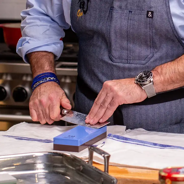 Home cook sharpening a Shun knife on a whetstone at a kitchen counter, demonstrating traditional at-home sharpening.