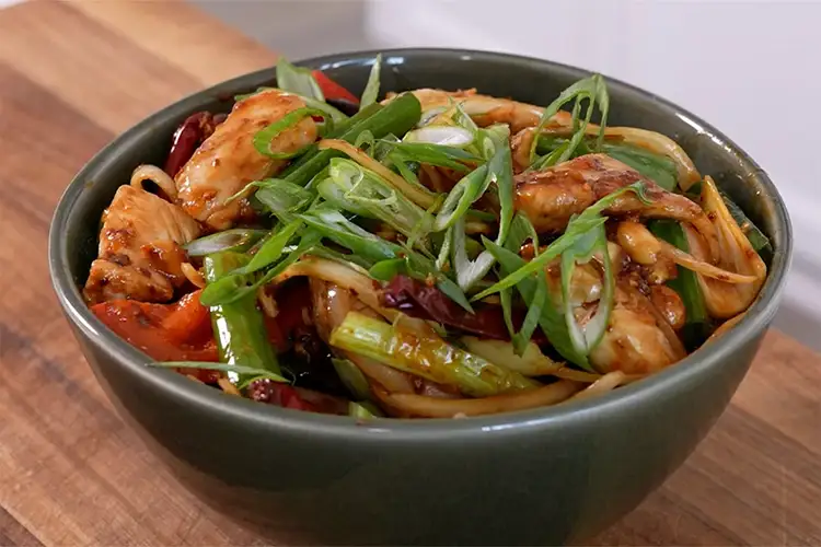 Chili crisp chicken in a bowl with sliced scallions on top