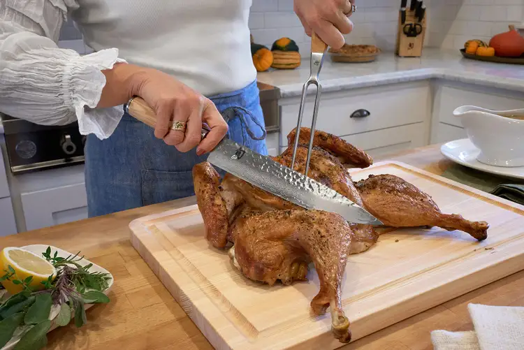 Carving into a roasted turkey using the Shun Premier Blonde Carving Knife and Fork on a wooden cutting board.