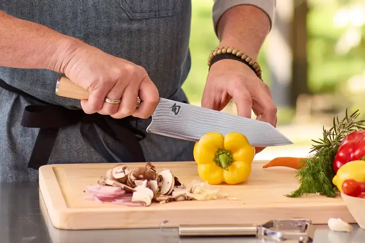 Chef demonstrating proper grip with a Shun Classic Blonde Kiritsuke over a yellow bell pepper on a wooden cutting board. Click to shop this knife.