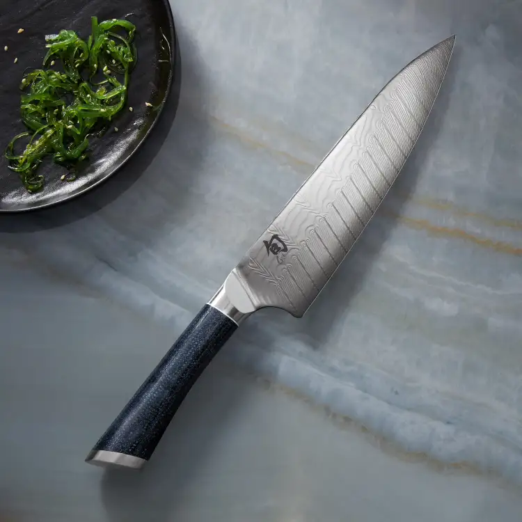 Shun Shiranami knife displayed with seaweed salad, showcasing the Damascus blade pattern and refined blade profile.
